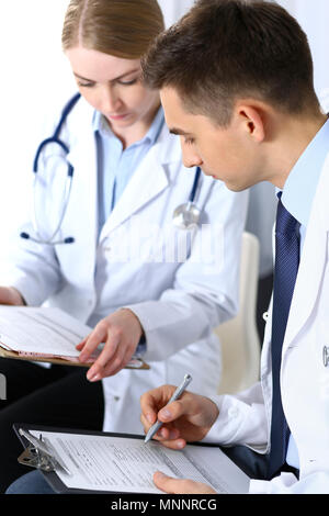 Doctors writing papers using clipboard. Physicians discussing medication program or studying at medical conference. Healthcare, insurance and medicine concept Stock Photo