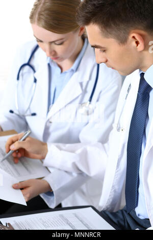 Doctors writing papers using clipboard. Physicians discussing medication program or studying at medical conference. Healthcare, insurance and medicine concept Stock Photo