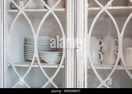 Plates, bowls, and tea cups stacked neatly in a vintage cabinet. Stock Photo