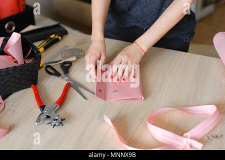 Female person making pink leather wallet with tools at atelier. Stock Photo