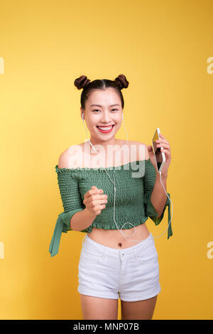 Fashion smiling asian woman listening to music in earphones  over yellow background Stock Photo