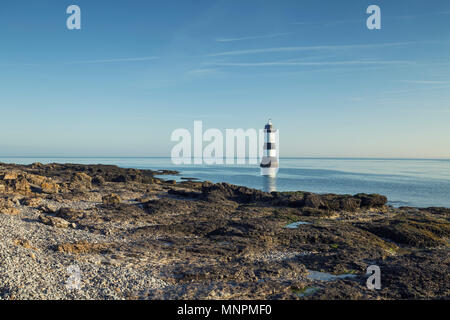 Penmon Point lighhouse on blue sky and low tide rocks. Anglesey, North Wales, UK Stock Photo