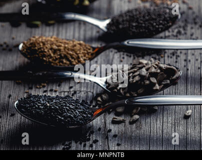 Close-up shot of metal spoons filled with black sesame and sunflower seeds on wood Stock Photo