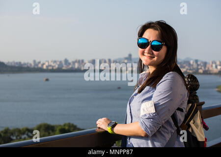 A beautiful Chinese lady wearing shade smiling posing at Leifong Pagoda, the background is West Lake in Hangzhou, China. Stock Photo
