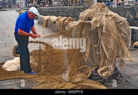FISHERMAN REPAIRING FISHING NETS. HONFLEUR, NORMANDY, FRANCE, JUNE 2014. Local fisherman repairing his fishing nets on the Quayside at Honfleur, Norma Stock Photo