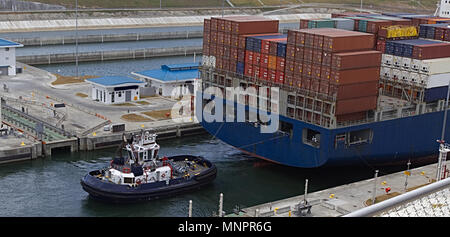 a tug boat works with a huge container ship in a canal to pull or push through Stock Photo