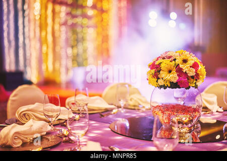 Wedding reception dinner table with flower bouquet decoration in the indian sangeet night with colorful lighting Stock Photo