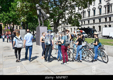 London street scene group of cycling tourists & tour guide with hire bikes people around statue of David Lloyd George in Parliament Square England UK Stock Photo