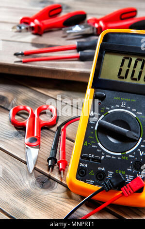 Multimeter, clamp, cable cutter, scissors and screwdrivers for working on a residential electrical system photographed on an antique wooden desk. Stock Photo