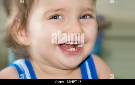 Close up shot of beautiful blue eyed baby happily and contagiously laughing showing its milk teeth. Shallow depth of field. Stock Photo