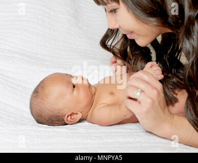 Baby boy laying on white blanket with mother holding his hands and smiling at him Stock Photo