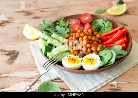 Buddha bowl, healthy and balanced food. Fried chickpeas, cherry tomatoes, cucumbers, paprika, eggs, spinach, arugula. Stock Photo