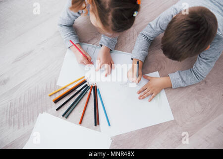 Children lie on the floor in pajamas and draw with pencils. Cute child painting by pencils Stock Photo