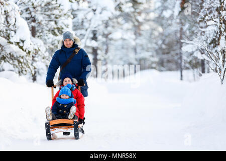 Beautiful family of father and kids enjoying snowy winter day outdoors having fun sledging Stock Photo