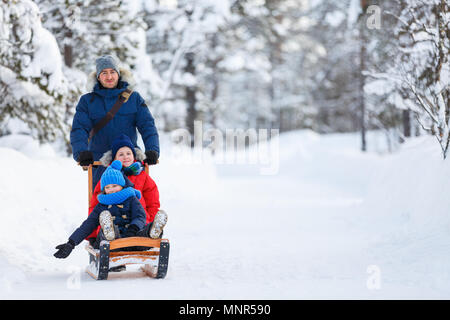 Beautiful family of father and kids enjoying snowy winter day outdoors having fun sledging Stock Photo