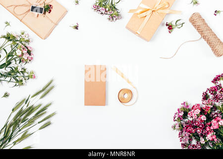 Packing gifts and preparing for celebration in process, top view. Flat lay composition blank cardboard box and coil of satin ribbon among pink flowers Stock Photo