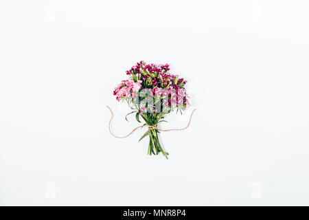 Simple flat lay arrangement of tiny pink flowers tied with twine. Top view composition of small bouquet in the center of white background. Stock Photo