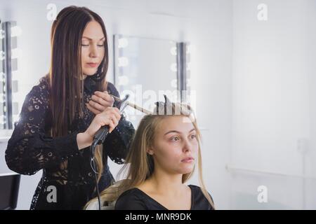 Beautiful young woman is getting her hair straightened at beauty saloon Stock Photo