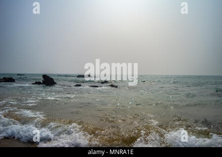 Beautiful rocky sea shore at sunrise or sunset Wild Empty Tropical beach, bright blue sky, crystal clear waters with water crashing on the shore. Stock Photo