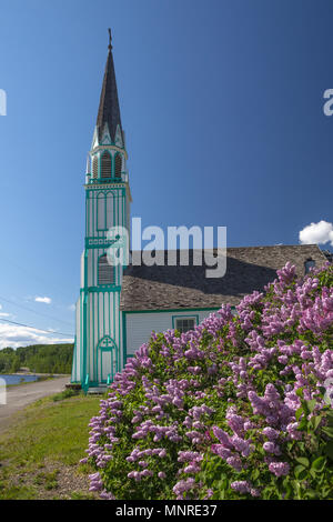 With vibrant blooming lilac in foreground, unique/y painted church of Our Lady of Good Hope in Fort St. James, Northern BC, sits on quiet road by lake Stock Photo