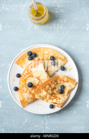 Crepes with blueberries and honey. Homemade pancakes, crepes on blue table, copy space. Stock Photo