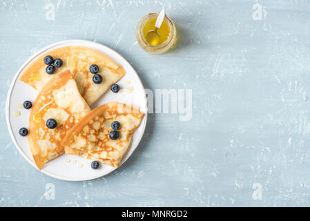 Crepes with blueberries and honey. Homemade pancakes, crepes on blue table, copy space. Stock Photo