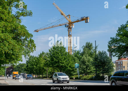 Cars on road with tall yellow crane in the background behind trees Stock Photo