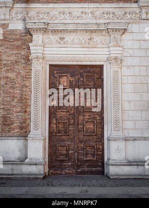 Old wooden portal with columns and architrave in white stone carved with floral motifs. Stock Photo