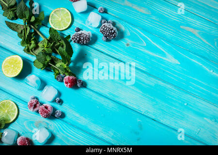 fresh berries, lime, mint and ice cubes on blue wood background. Copyspace Stock Photo