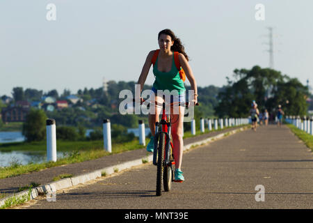 Girl riding a bike in the city, illuminated by sunlight Stock Photo