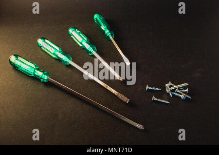Green screwdrivers and screws on dark grey background Stock Photo