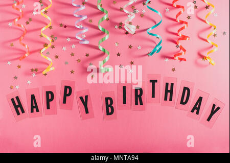 Colorful party streamers, gold little stars and text Happy Birthday on pink background. Girly birthday concept. Flat lay. Stock Photo