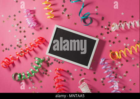 Colorful party streamers, gold little stars and blackboard for text on pink backgrond. Party or birthday concept. Stock Photo