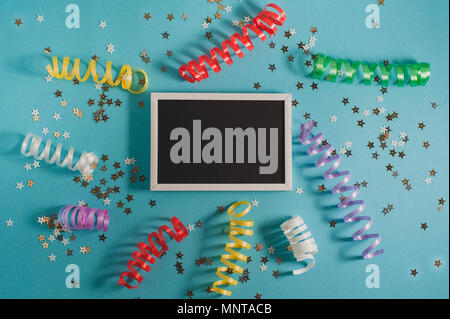 Colorful party streamers, gold little stars and blackboard for text on blue backgrond. Party or birthday concept. Stock Photo