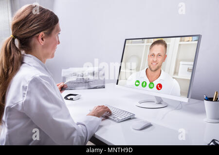 Dentist Holding Teeth X-ray While Video Conferencing With Man On Computer Stock Photo