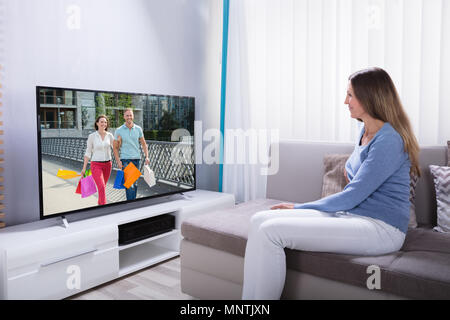 Woman Lying On Sofa Using Calculator While Watching Television At Home Stock Photo