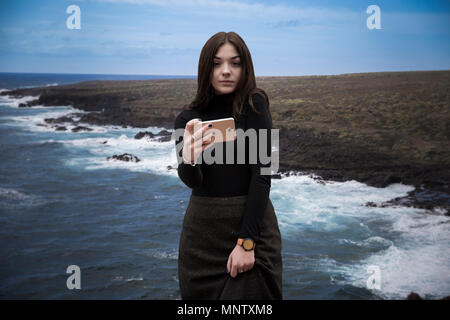 girl is making a selfie on the edge of a cliff in the background of the ocean Stock Photo