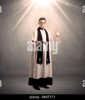 A male religious young priest in black and white dress giving his blessing, holding the holy bible while being illuminated from strong light beams coming from above concept