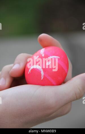 Bright pink angry Easter egg in a child's hand on Easter morning. Stock Photo