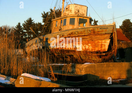 The setting sun illuminates an abandoned boat ashore in Onset, Massachusetts, USA Stock Photo