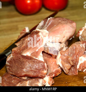 Raw meat. Raw fillet beef or pork, cut in large pieces, knife and tomatoes. Ready for cooking. Lies on wooden table. Square. Close-up. Stock Photo