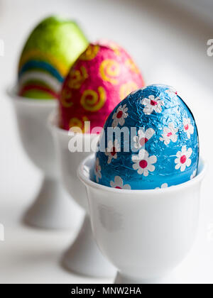 Chocolate Easter Eggs in egg cups: A row of three eggs in three white porcelain egg cups on a white background. Stock Photo