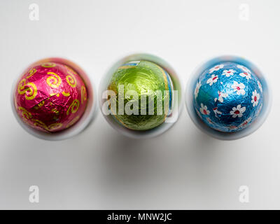 Chocolate Easter Eggs in egg cups: A row of three eggs in three white porcelain egg cups on a white background. Stock Photo