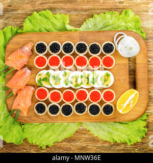 Homemade tartlets with red and black caviar, salmon, lettuce and eggs. On a cutting board. Concept of luxury food. Top flat view. Square. Close-up. Stock Photo