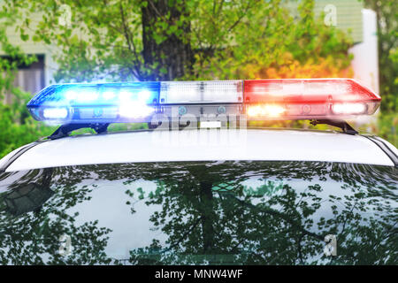 Colorful siren on the roof of a police car in a real operation. Red and blue light flasher of a police car with blurred street at background. Stock Photo