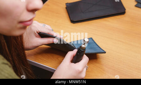 Tanner grinds edges of leather purse. Handmade. Workflow in workshop. Shooting close-up. Stock Photo