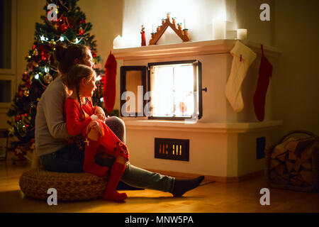Mother and daughter sitting by a fireplace in their family home on Christmas eve Stock Photo