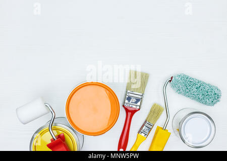 cans with white, orange and yellow paint, brushes, rollers on white wooden surface flat view Stock Photo