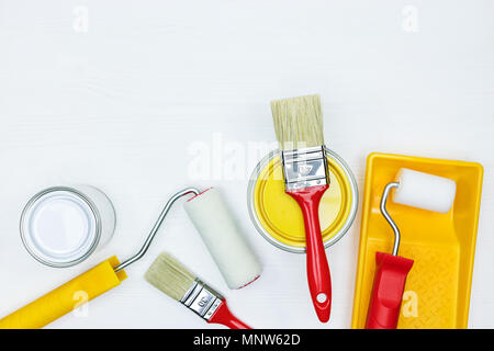 paint cans with rollers, brushes and paint tray on white wooden desk background. flat view Stock Photo
