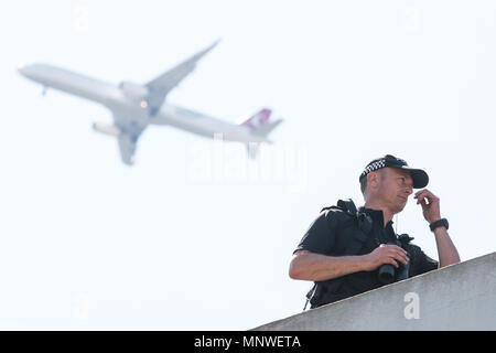 Windsor, UK. 19th May, 2018. A plane from Heathrow airport flies high above a police officer on a rooftop above the High Street observing thousands of well-wishers lining the streets of Windsor to witness the carriage procession of Prince Harry and Meghan Markle, now the Duke and Duchess of Sussex following their wedding at St George's Chapel in Windsor Castle. Credit: Mark Kerrison/Alamy Live News Stock Photo